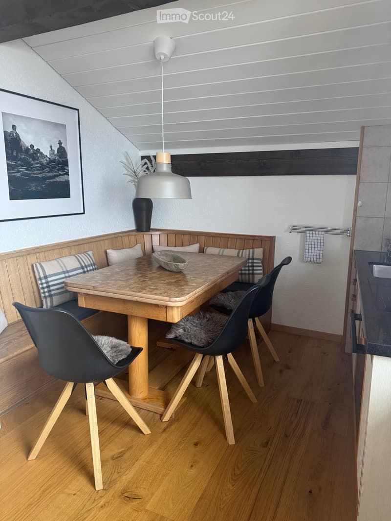 Dining area with a wooden table, black chairs, built-in bench seating, and a modern pendant light.