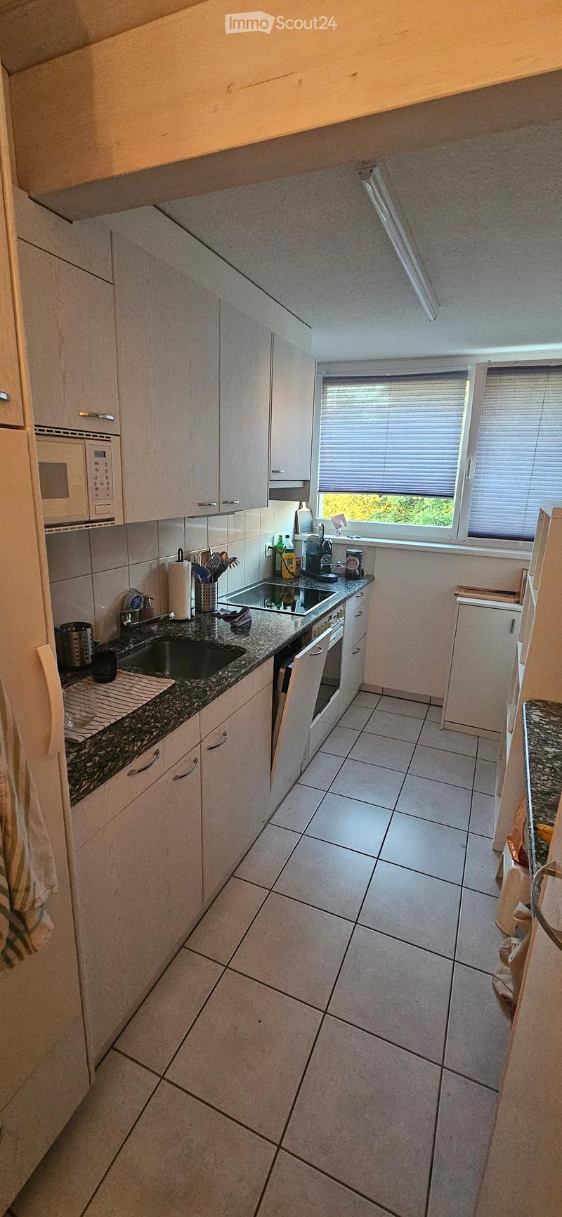 Modern kitchen with white cabinets, granite countertops, tiled floor, microwave, sink, oven, and coffee maker.