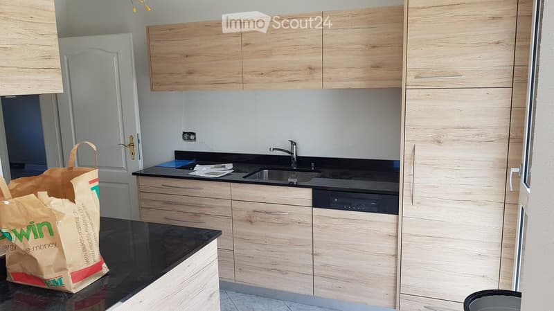 Modern kitchen with light wooden cabinets, black countertops, and stainless steel sink and dishwasher.