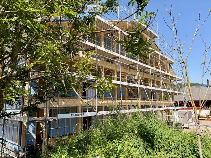 Multi-story building under construction with scaffolding, visible wooden beams, and construction materials.