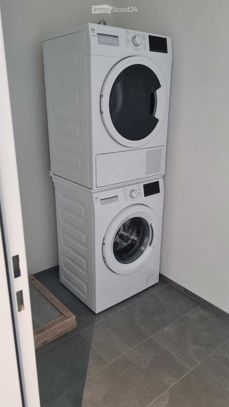 A small bathroom with a stacked washing machine and dryer unit against the wall, featuring a tiled floor and light-colored walls.