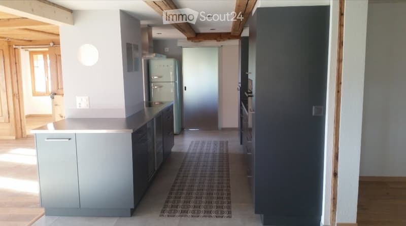 Modern kitchen with grey cabinets, a white countertop, and a vintage-style refrigerator. Exposed wooden beams on the ceiling and a patterned rug on the floor.