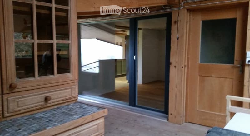 A wooden hallway with a sliding glass door leading to another room, wooden cabinetry, and a small bench.