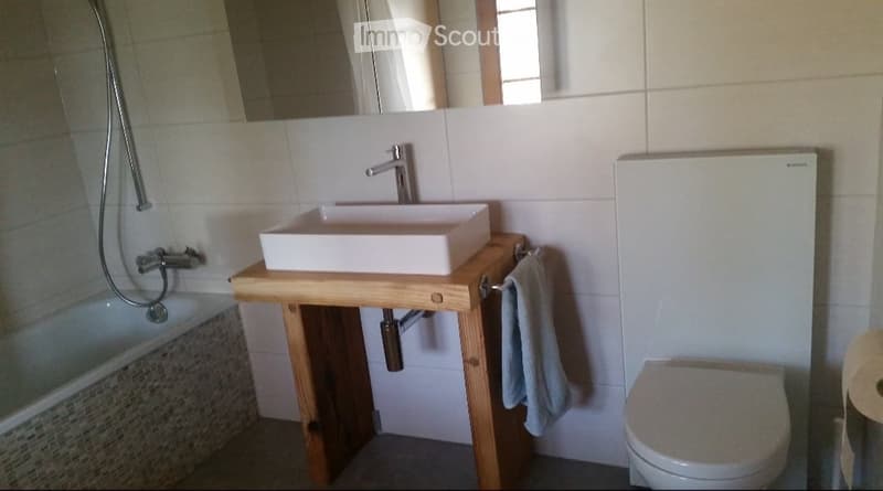 Modern bathroom with a wooden sink console, white sink, chrome faucet, towel rack, toilet, and bathtub.