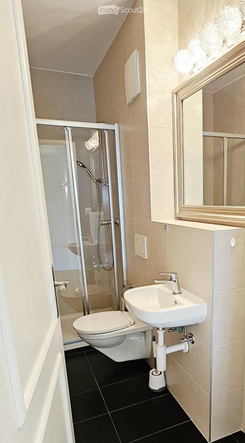 Modern bathroom with black tiled floor, white toilet, sink, and shower stall. Features a large mirror above the sink and a window with frosted glass.