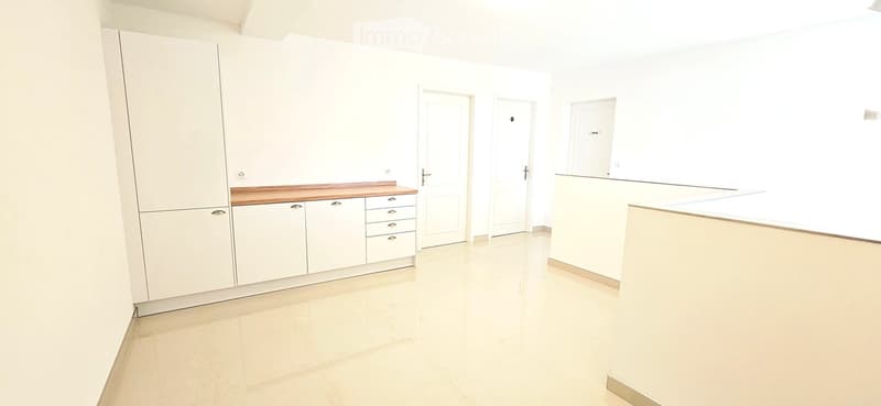 Empty room with white walls, light-colored tiled floor, and built-in white cabinetry with a wooden countertop. Three doors are visible.