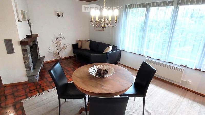 Living room with a dark leather sofa, wooden coffee table, fireplace, chandelier, and decorative vase with pinecones.