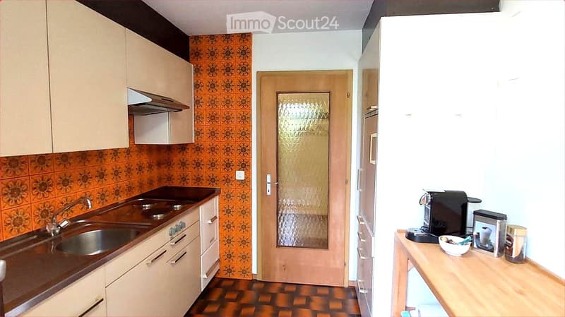 The kitchen features a sink with a faucet, wooden cabinets, a refrigerator, and a coffee maker on the counter.