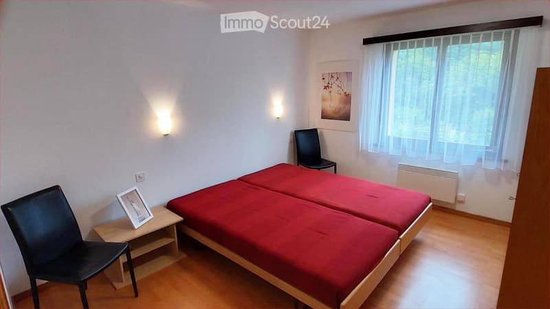 Cozy bedroom with two single beds, red bedding, wooden floor, wall-mounted lamps, and a nightstand with a picture frame.