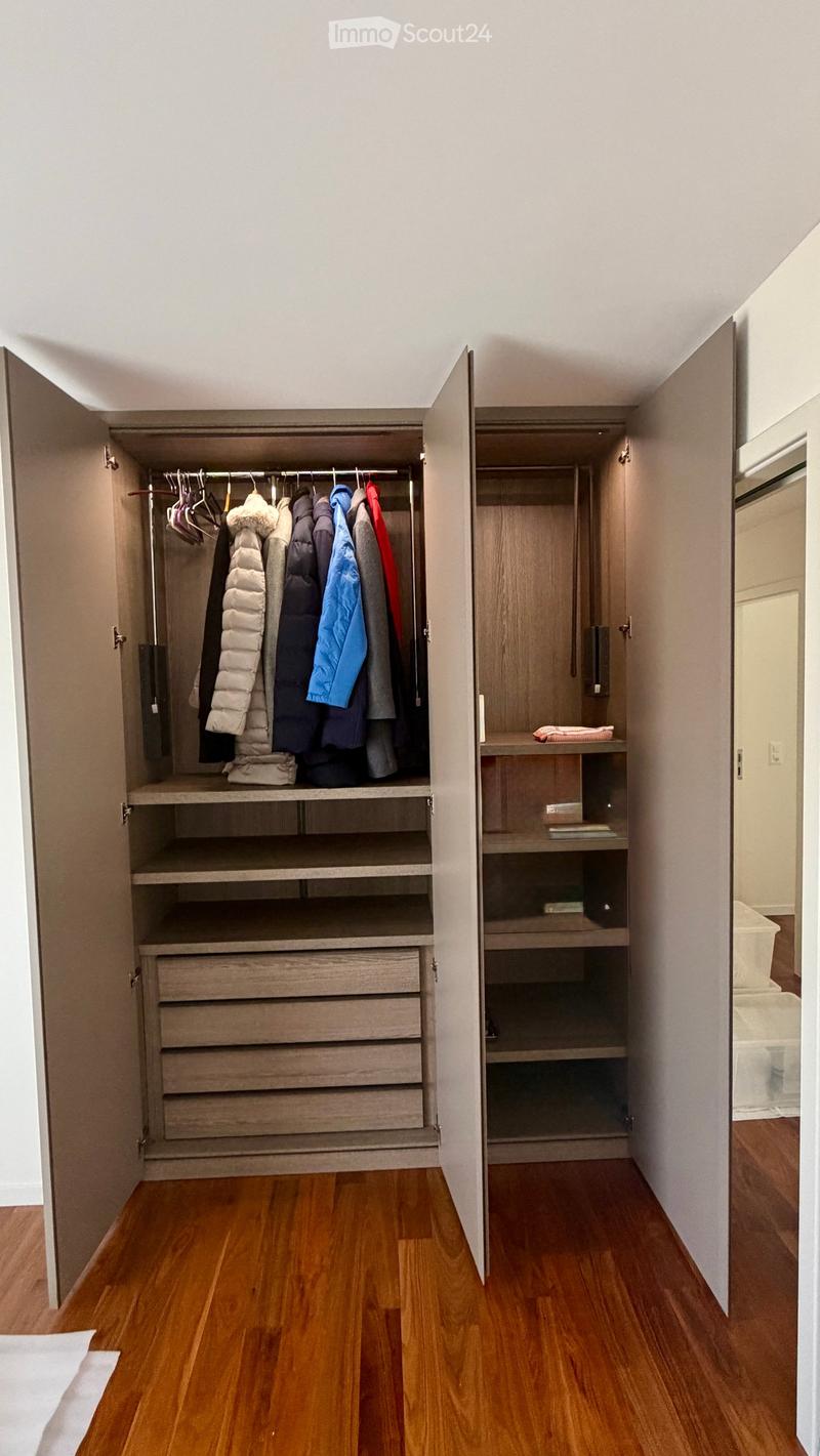 Open wardrobe with multiple sections including hanging space, shelves, and drawers, located in a room with wooden flooring.
