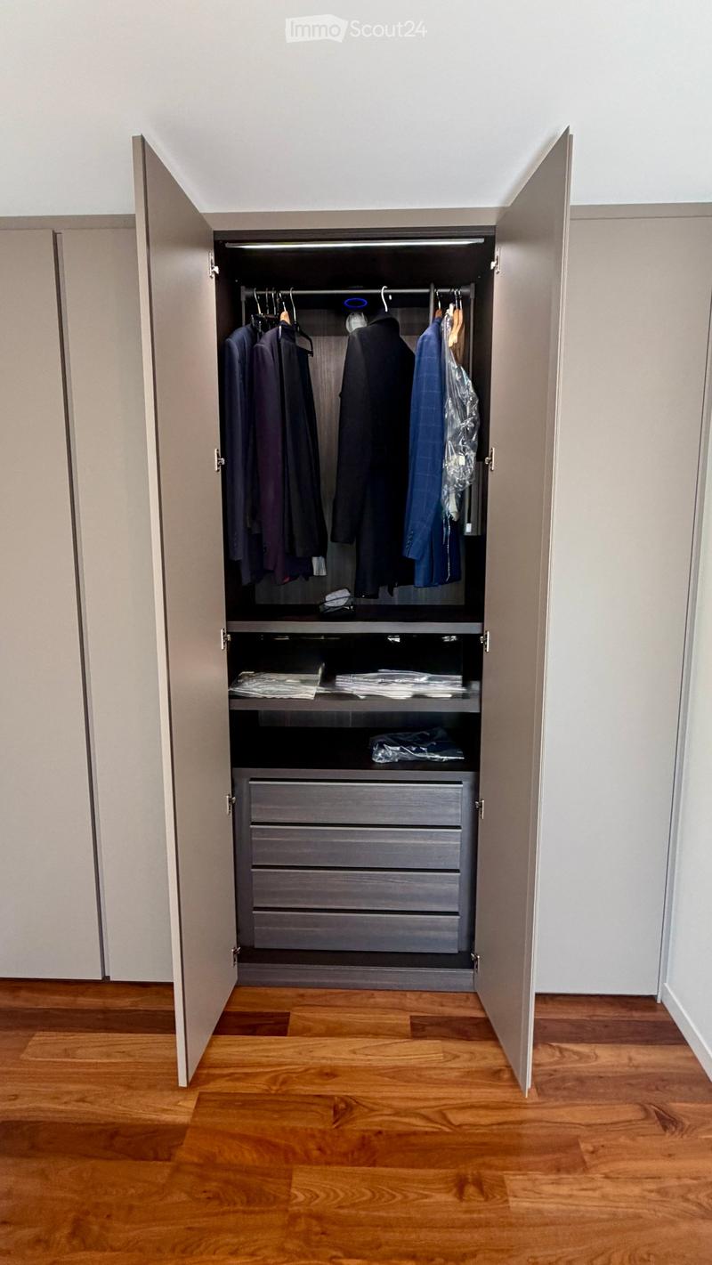 An empty room with wooden flooring and a large, open wardrobe with multiple hanging rods and drawers, but no visible furniture or personal items.