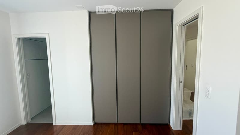 Empty room with white walls, wooden flooring, and a large closet with sliding doors. Two doorways lead to other rooms.