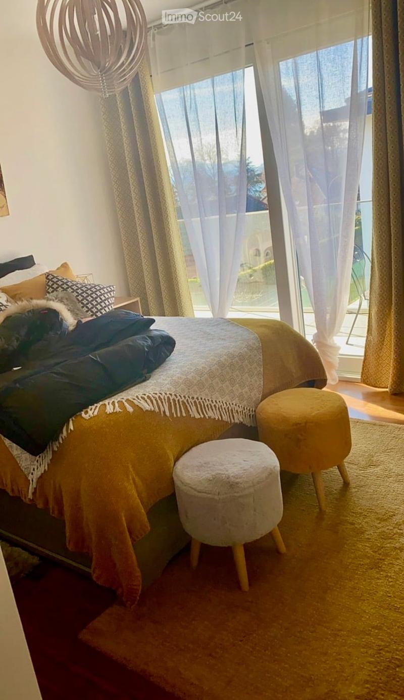 Cozy bedroom with a large bed, yellow and white bedding, two round stools, and sheer curtains covering a large window.
