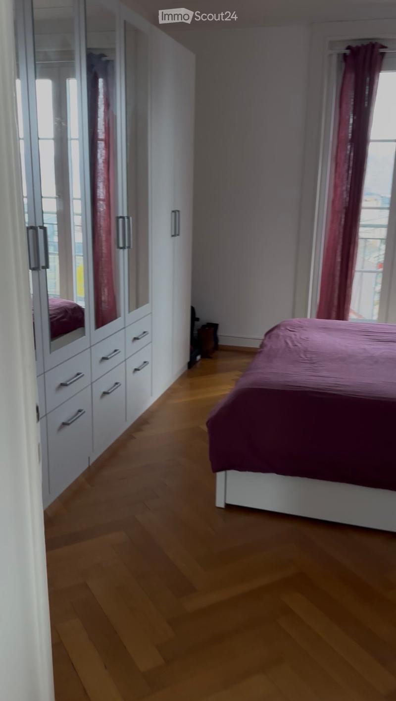 Spacious bedroom with wooden flooring, a neatly made bed with a pink duvet, and a large white wardrobe with mirrored doors.