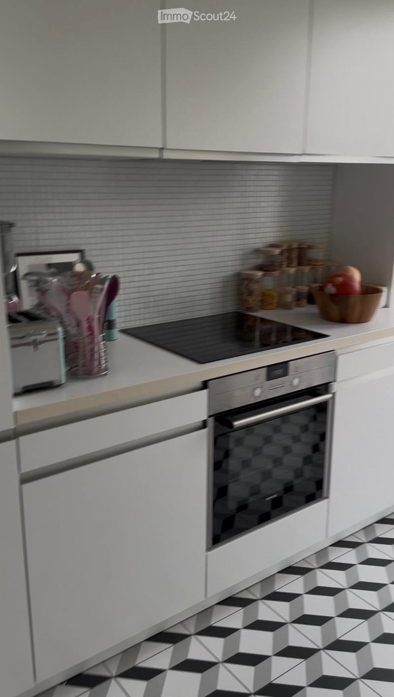 Modern kitchen with white cabinets, black and white tiled floor, stainless steel oven, countertop with various items including a bowl and jars.