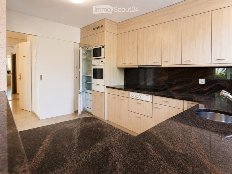 Modern kitchen with light wooden cabinets, granite countertops, stainless steel sink, and built-in appliances including a refrigerator, microwave, and oven.