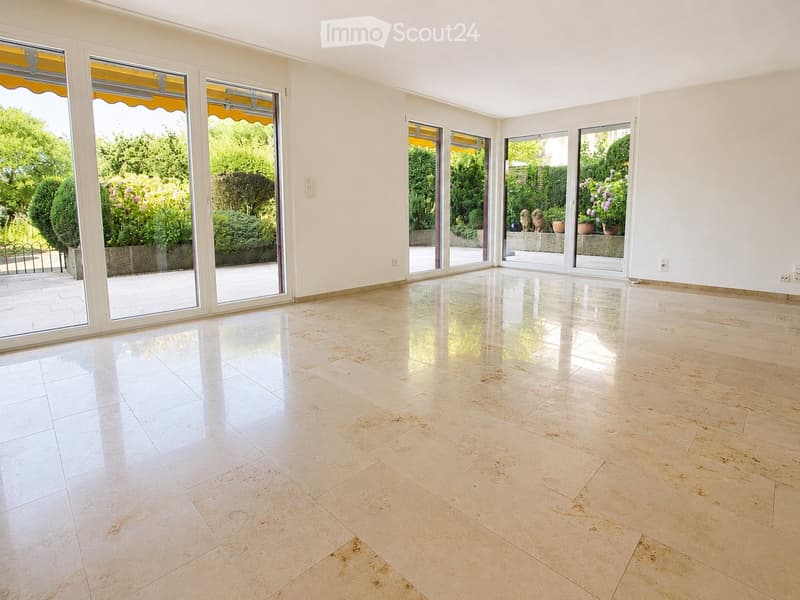 Empty room with large sliding glass doors leading to a garden, polished tile floor, white walls, and visible electrical outlets.