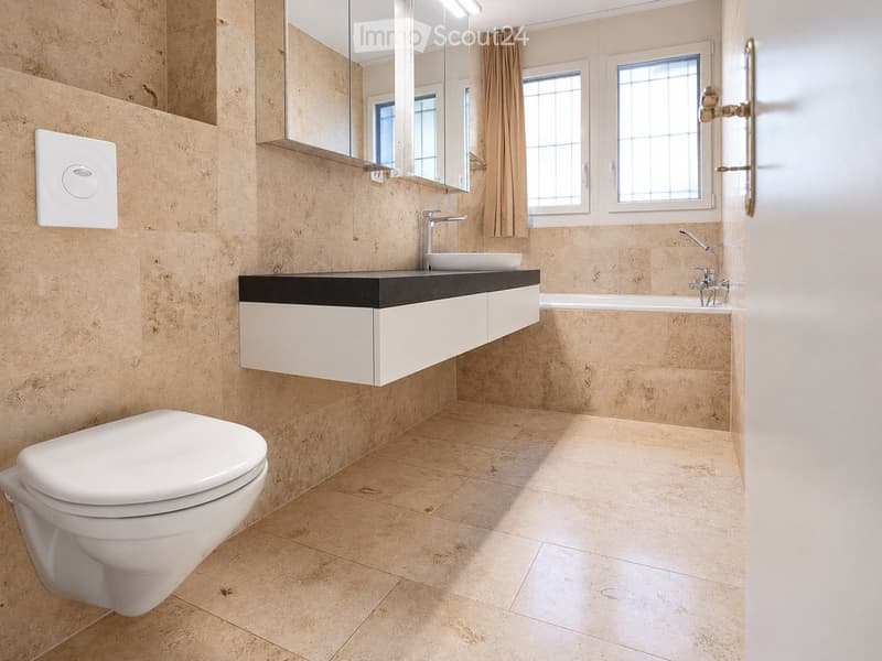 Modern bathroom with beige tiled walls and floor, white toilet, sink with chrome faucet, bathtub, and large mirror above the sink.