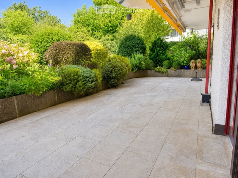 A well-maintained garden area with a tiled patio, lush greenery, and decorative elements such as statues and planters.