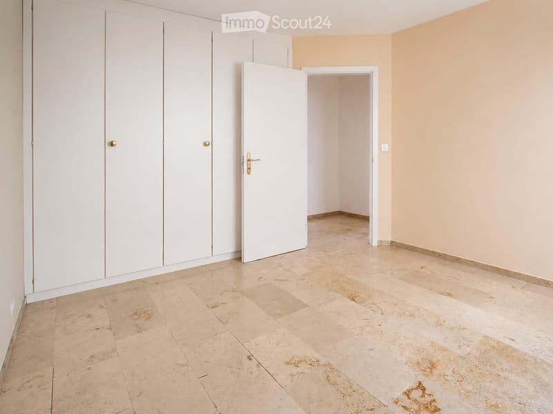 Empty room with beige tiled flooring, white walls, and built-in white closet units. A doorway leads to another room.