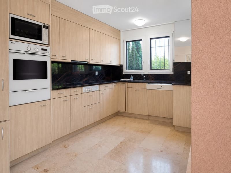 Modern kitchen with light wooden cabinets, stainless steel appliances, and tiled flooring.