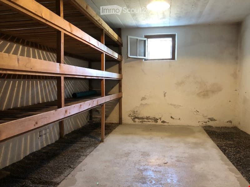 Empty room with wooden bunk beds, concrete floor, and a small window with an open vent. The walls are plain and show some wear.