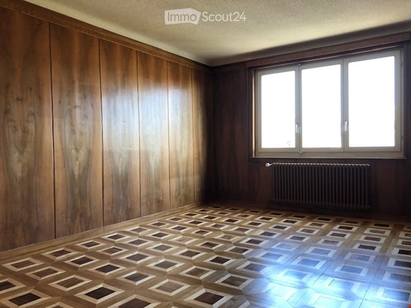 Empty room with wooden panel walls, geometric patterned tile floor, large window, and radiator.