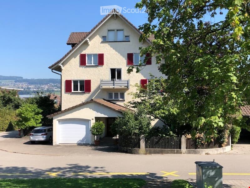 Two-story house with red shutters, white windows, garage, and driveway with a parked car.