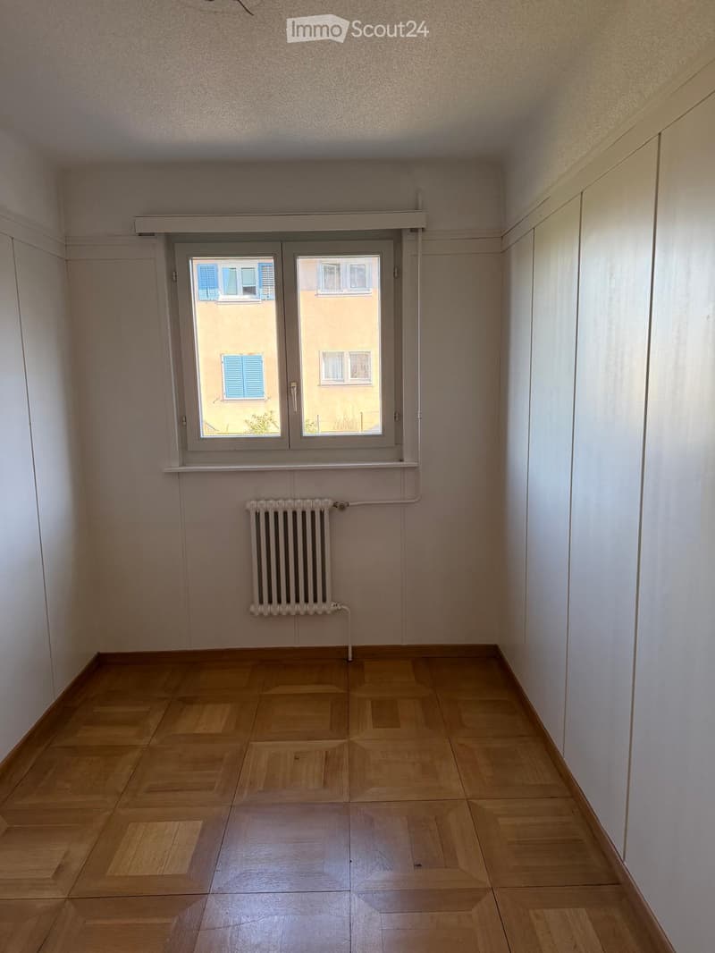 Empty room with wooden flooring, white walls, a window with shutters, and a radiator below the window.