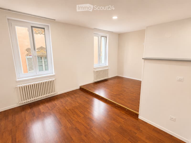 Empty room with wooden flooring, white walls, and two windows with radiators beneath them.
