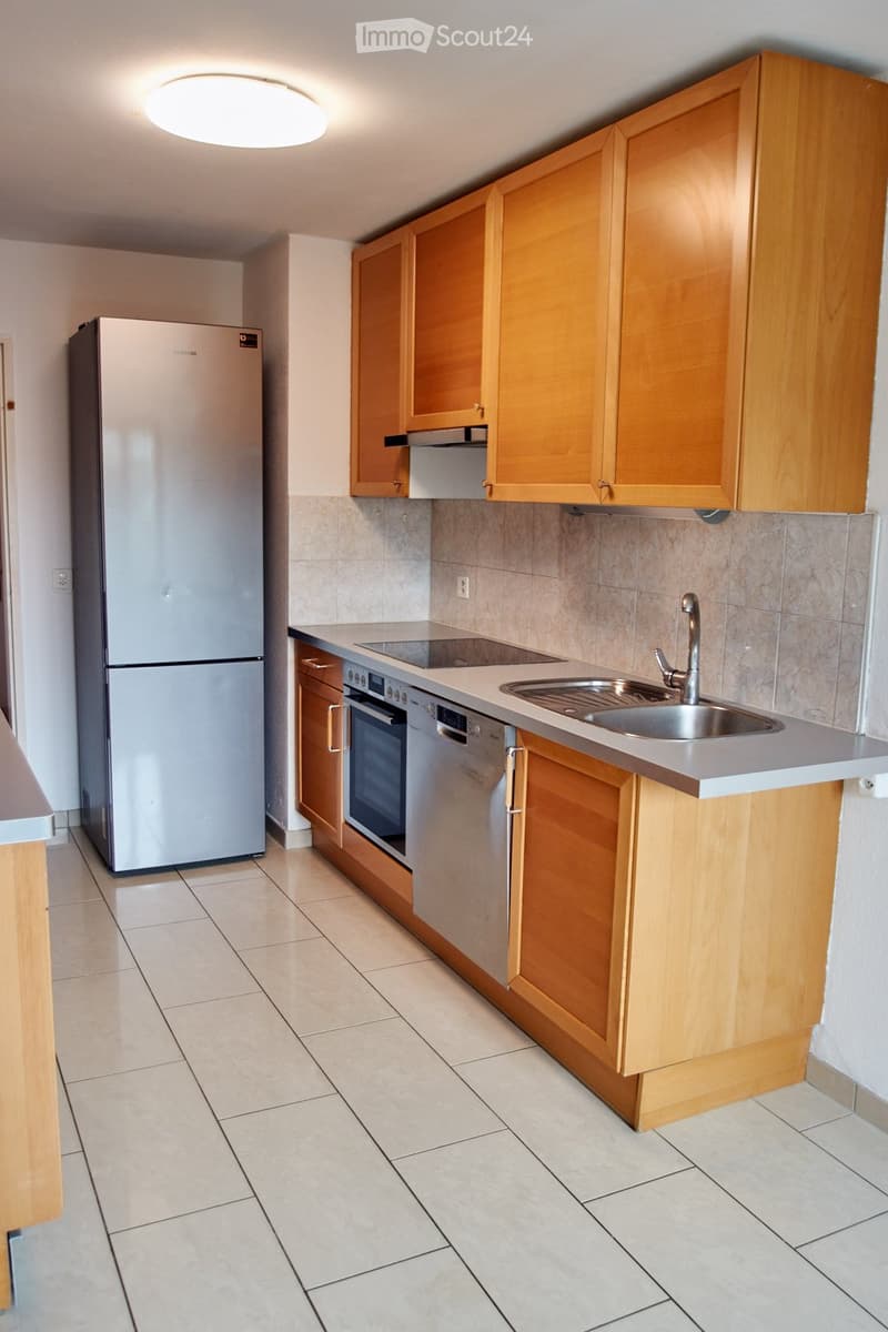 Modern kitchen with light wooden cabinets, stainless steel appliances, and a tiled floor.