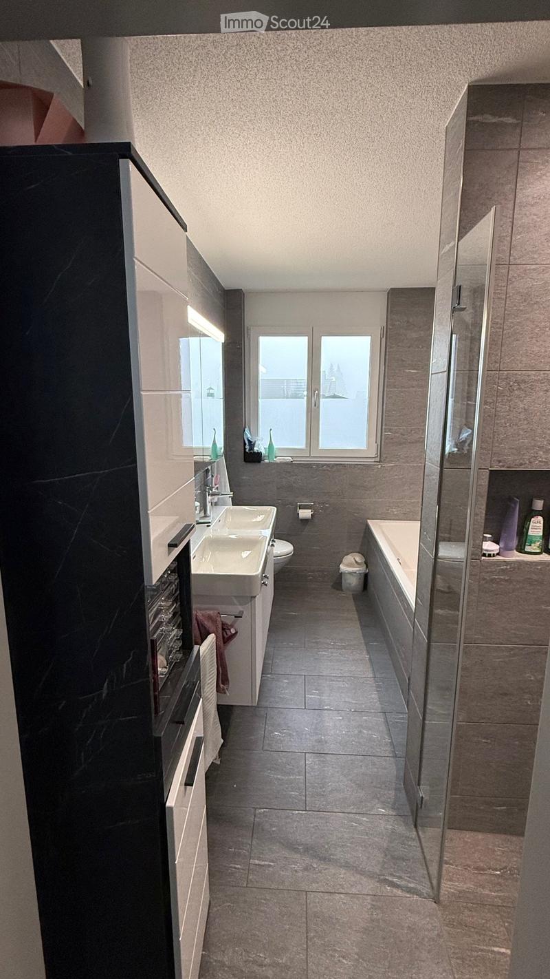 Modern bathroom with double sink, toilet, bathtub, and large windows offering a view.