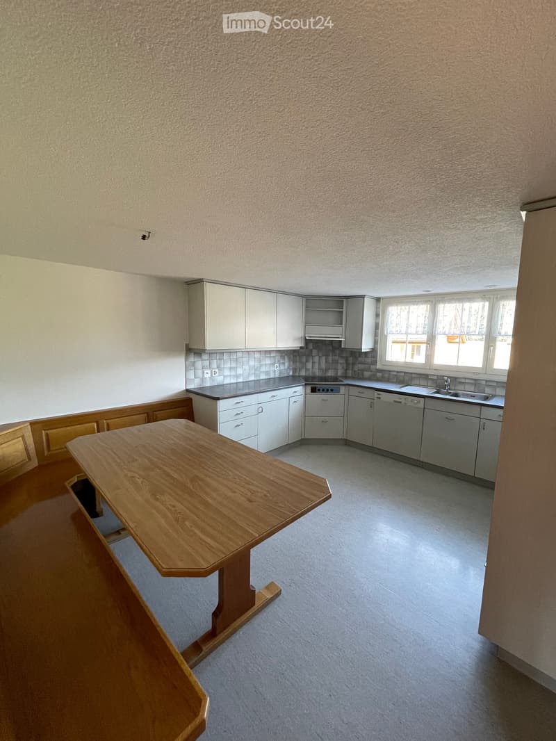 Modern kitchen with white cabinets, a wooden dining table, and built-in appliances including a dishwasher and sink.