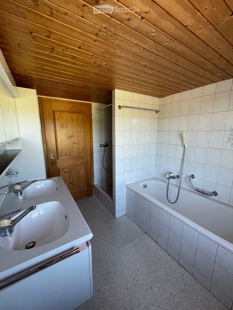 Bathroom with double sink, bathtub, and wooden door leading to another room.