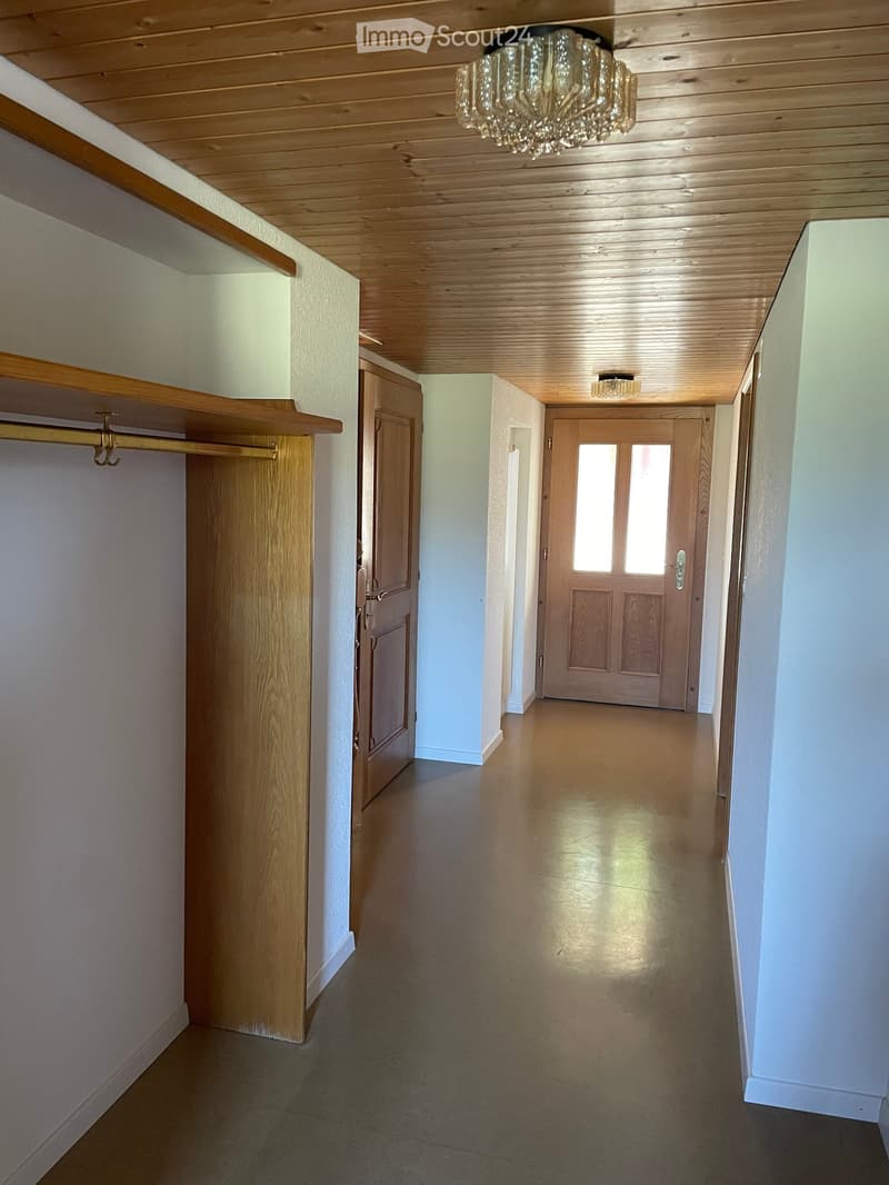 Empty hallway with wooden ceiling, light-colored walls, and wooden doors. Features built-in wooden shelving on one side and a chandelier hanging from the ceiling.
