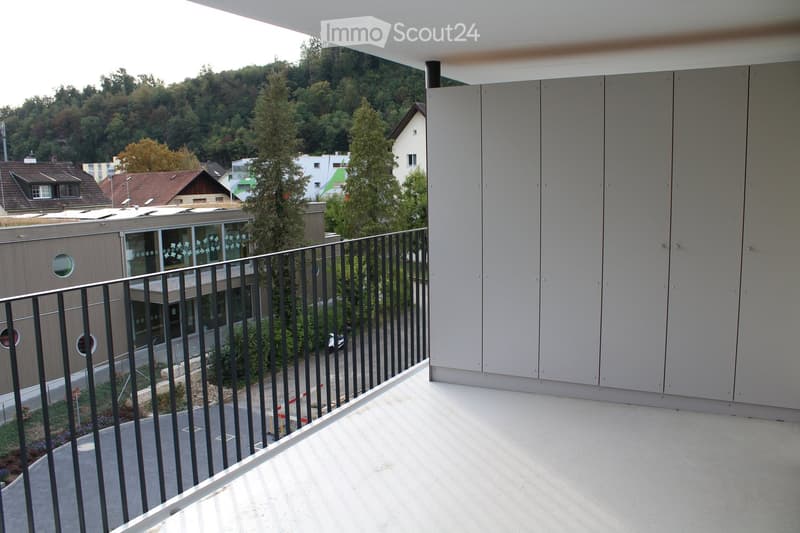 Modern balcony with metal railing, concrete floor, and expansive view of surrounding greenery and buildings.