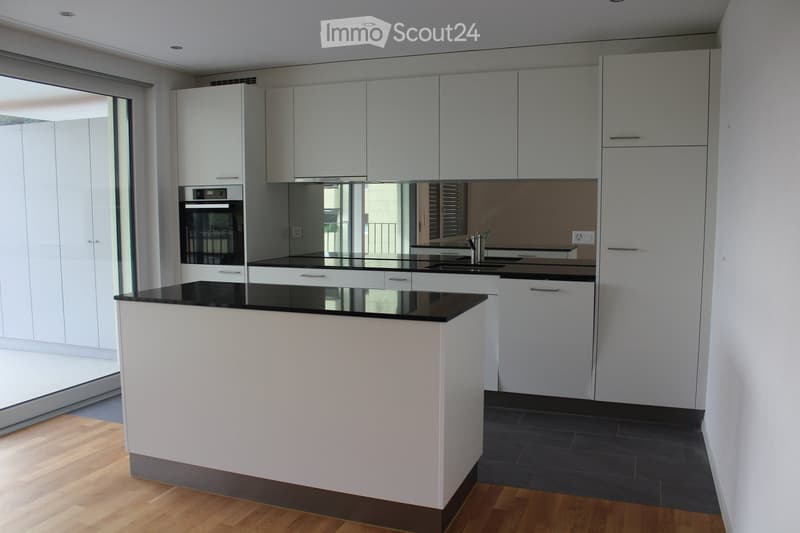 Modern kitchen with white cabinets, black countertops, and a central island. Features an oven, sink, and ample storage space.