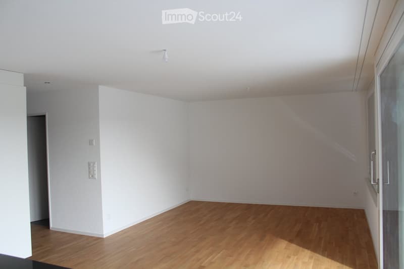 Empty room with light wooden flooring and white walls, featuring a large glass door and a small doorway leading to another space.