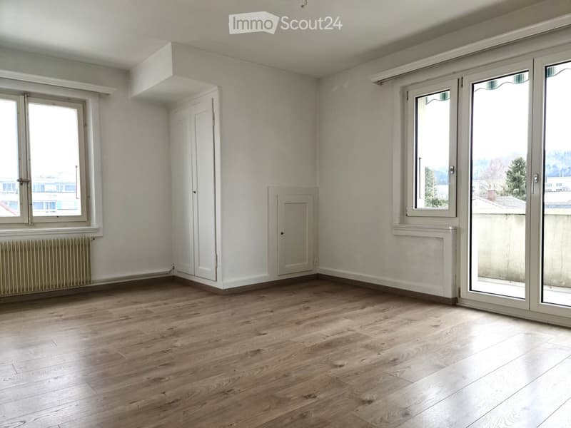 Empty room with wooden flooring, white walls, and large windows with sliding doors, featuring a radiator and a small closet.