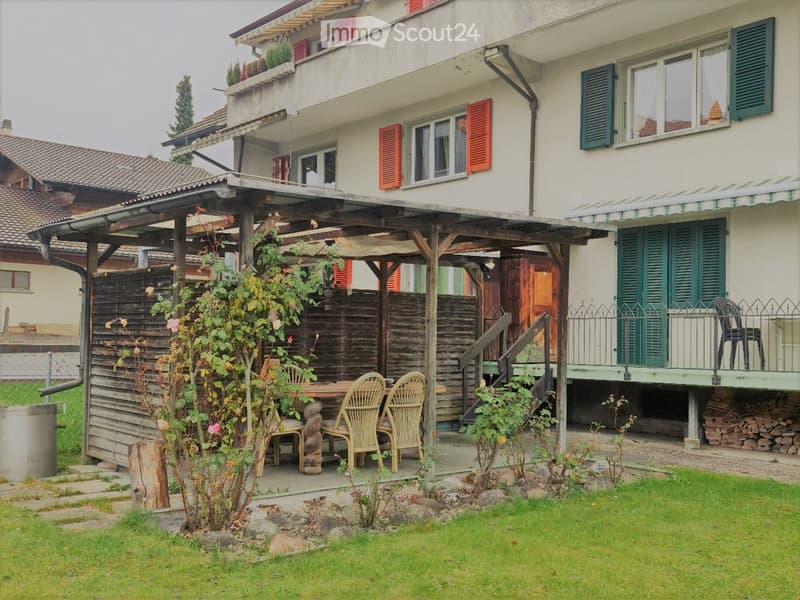 A two-story house with a covered patio area, outdoor furniture, and a well-maintained garden.