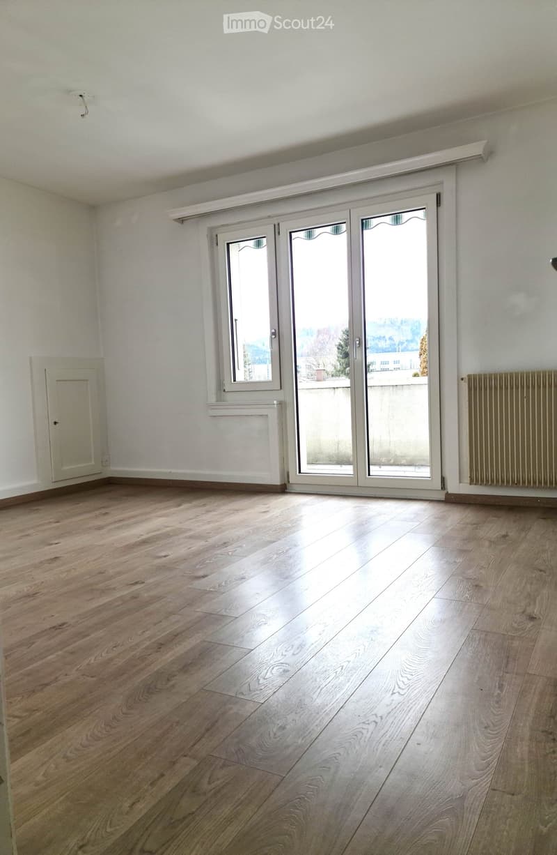 Empty room with light wooden flooring, white walls, and large sliding glass doors leading to a balcony.
