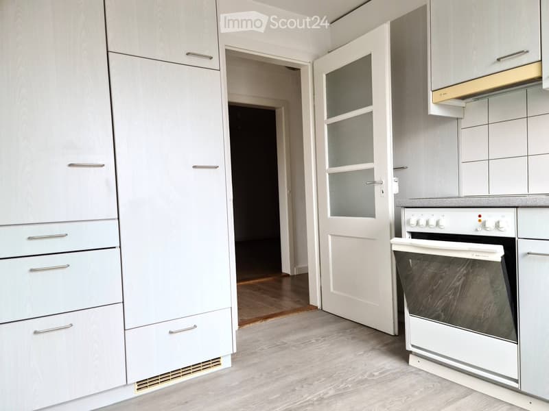Modern kitchen with white cabinets, a built-in oven, and a light wooden floor.