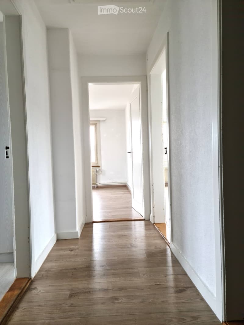 Empty hallway with wooden flooring and white walls, featuring several doors leading to other rooms.