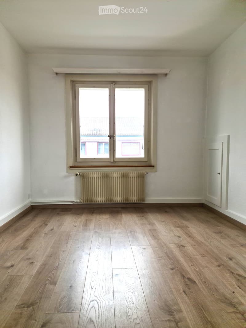 Empty room with light wooden flooring, white walls, a window with double panes, and a radiator below the window.