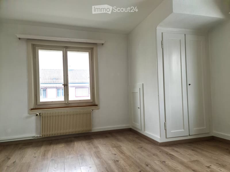 Empty room with wooden flooring, white walls, a window with a radiator below, and a white closet.