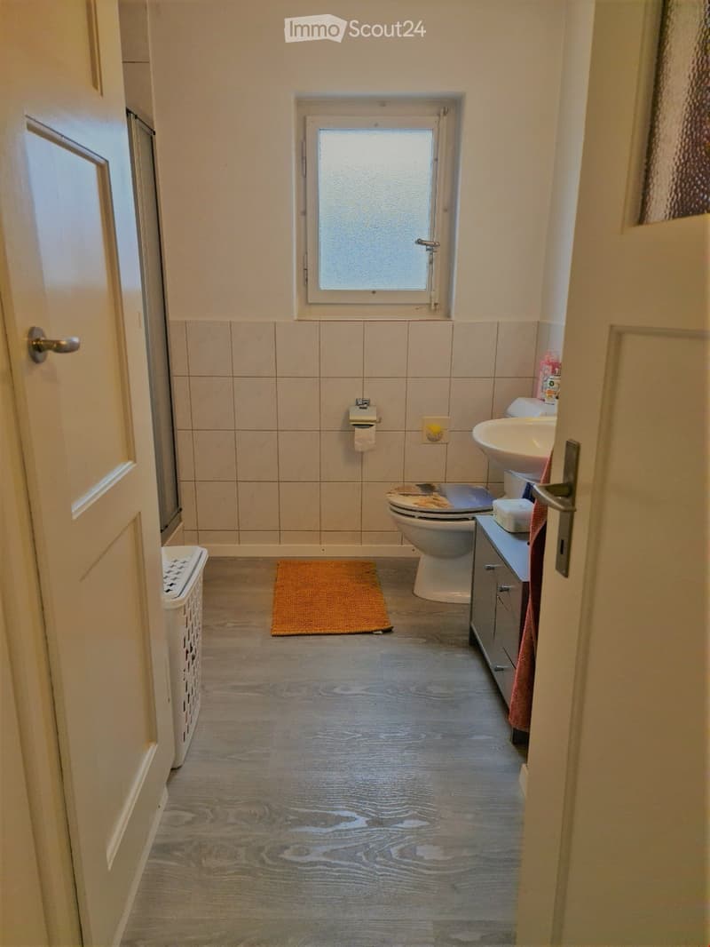 Bathroom with wooden flooring, tiled walls, toilet, sink, cabinet, and a small window above the toilet.