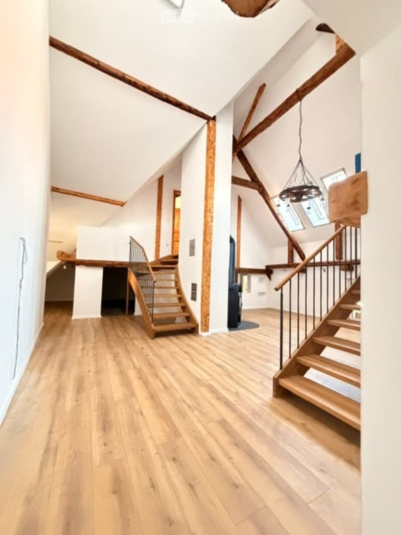 Bright, airy hallway with wooden floors, exposed wooden beams, and two staircases leading to different levels.