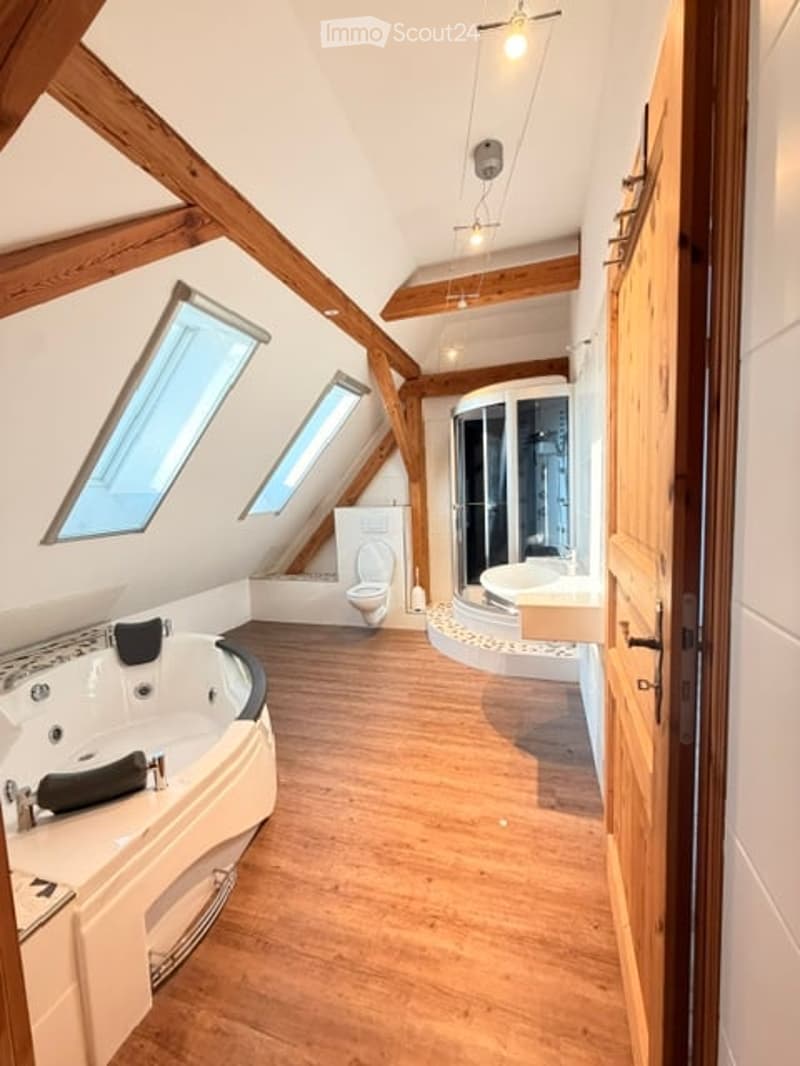 Modern bathroom with wooden beams, skylights, a bathtub, toilet, sink, and a walk-in shower.