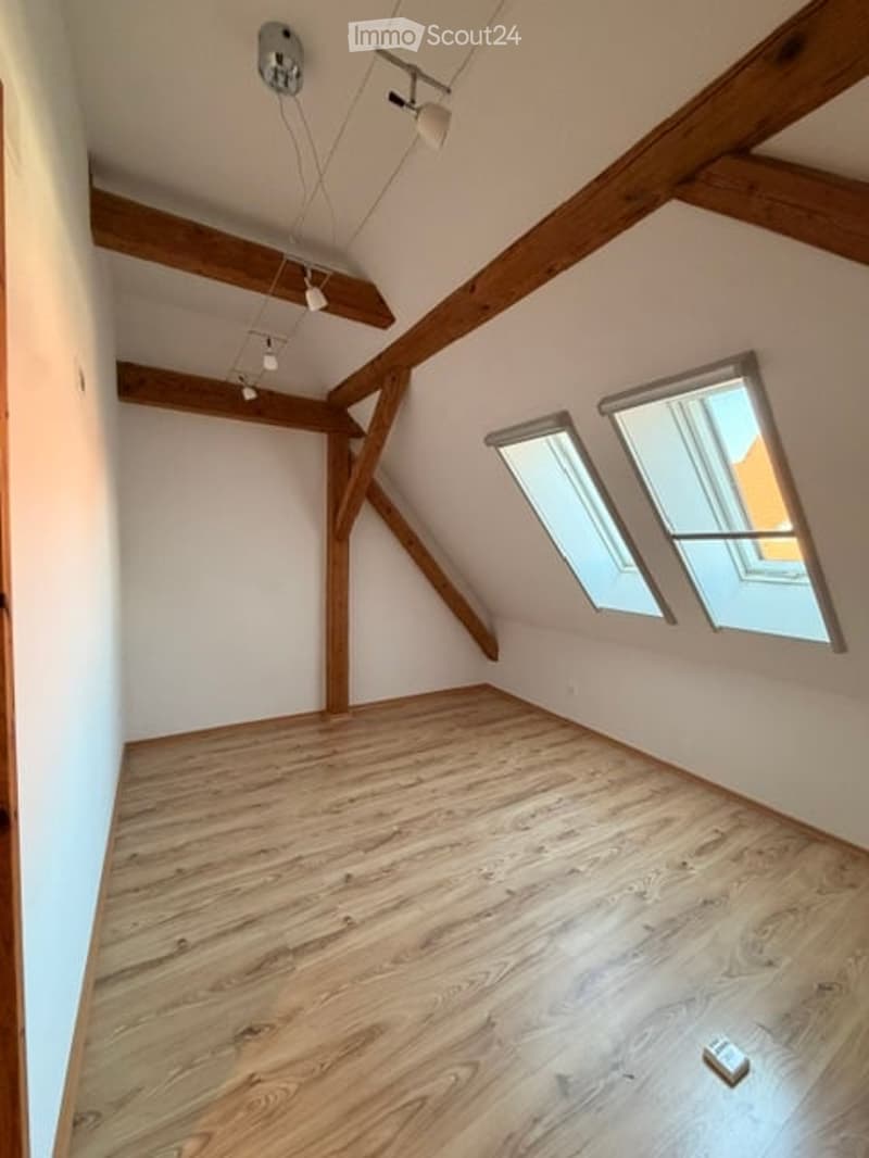 Empty attic room with wooden beams, wooden floor, and skylight windows.