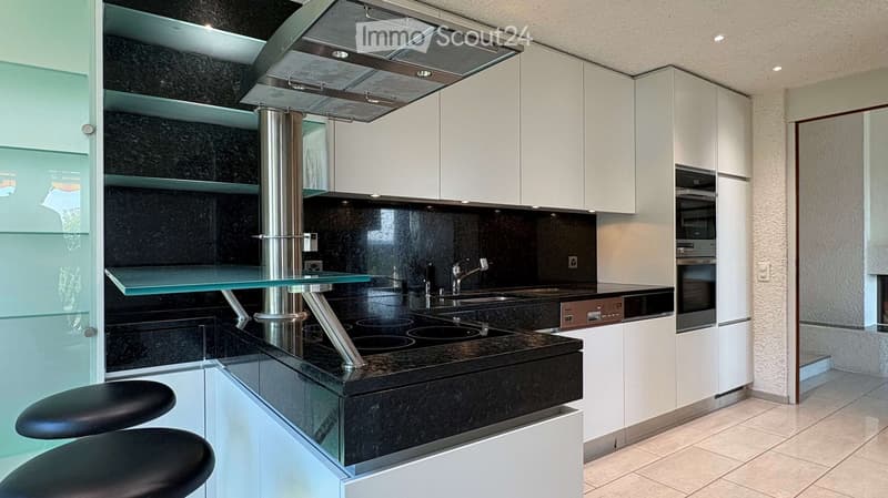 Modern kitchen with white cabinets, black granite countertops, stainless steel appliances, and a glass island with black stools.